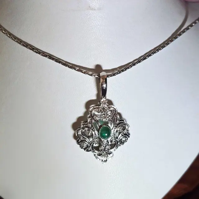 Um COLAR, pesando 16,60 gramas, em ouro branco 18 k, com treze BRILHANTES e uma ESMERALDA